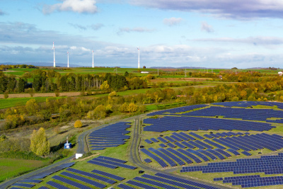 Freiflächen Solarfeld mit Windenergie im Hintergrund auf Hügeln und Wald im Hintergrund